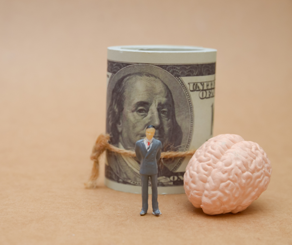 figurine of businessman standing next to a model of a brain and a roll of cash